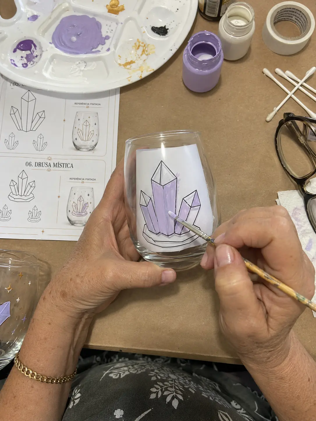 Mãos pintando cristais lilases na taça ao lado da cartela do molde
