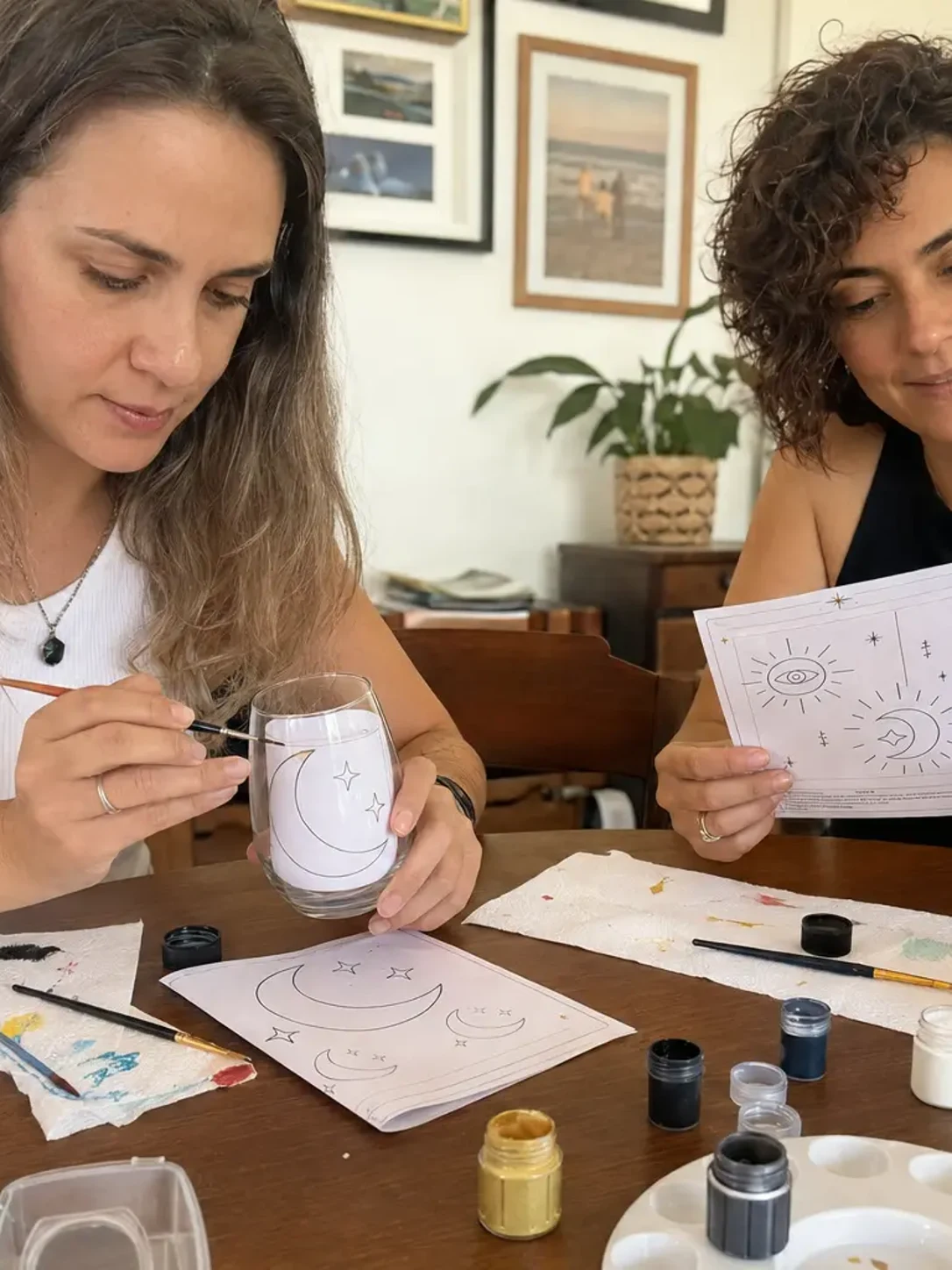 Duas amigas pintando taças com luas e estrelas usando os moldes